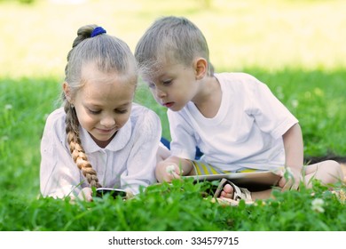 Happy children using tablet PC and smartphone laying on the grass. Brother and sister.