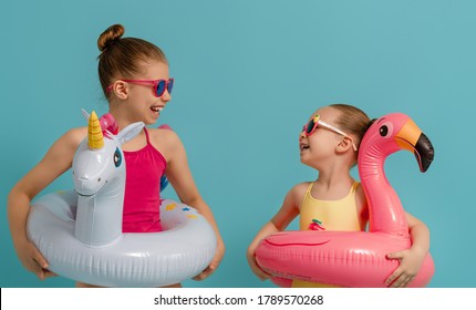 Happy children wearing swimsuit. Girls with swimming rings unicorn and flamingo. Kids on a colored turquoise background.