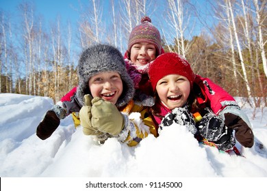Happy children in winterwear laughing while playing in snowdrift outside