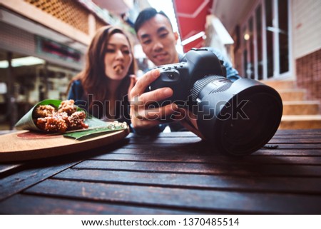 Happy chinese couple sitting at cafe outside enjoying traditional asian food and watching pictures in photo camera. Widescreen shooting. Photo camera is in focus.