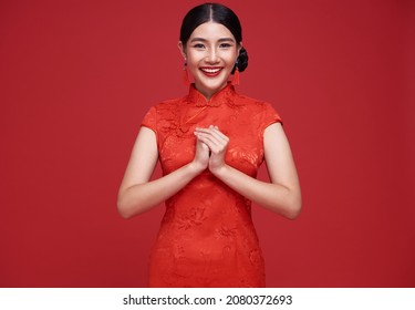 Happy Chinese new year. Asian woman wearing traditional cheongsam qipao dress with gesture of congratulation isolated on red background.