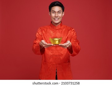 Happy Chinese New Year. Asian Man Wearing In Traditional Costume Holding Gold Ingot Isolated On Red Background.
