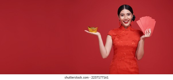 Happy Chinese new year. Asian woman holding angpao or red packet monetary gift and gold ingot isolated on red background. - Powered by Shutterstock