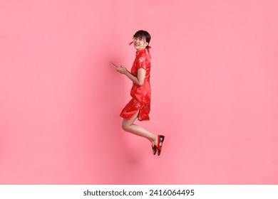 Happy Chinese new year. Asian Chinese woman wearing red traditional cheongsam qipao with gesture of Holding mobile phone isolated on pink background.