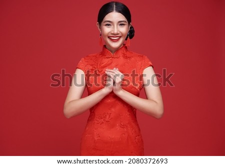 Happy Chinese new year. Asian woman wearing traditional cheongsam qipao dress with gesture of congratulation isolated on red background.