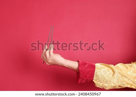 Happy Chinese new year. Asian Chinese energetic senior man wearing golden traditional cheongsam qipao or changshan dress with gesture of hand holding silver chopsticks isolated on red background.