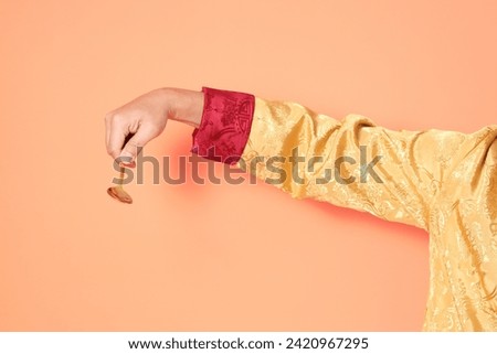 Happy Chinese new year. Hand of asian chinese senior man wearing golden traditional clothing with gesture of hand holding golden spoon isolated on orange background.