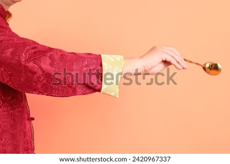 Happy Chinese new year. Hand of asian chinese senior man wearing red traditional clothing with gesture of hand holding golden spoon isolated on orange background.