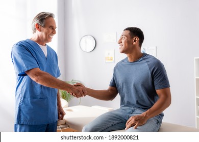 happy chiropractor shaking hands with african american patient - Powered by Shutterstock
