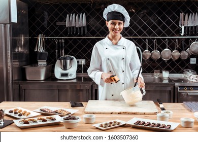 Happy Chocolatier In Chef Hat Holding Cooking Thermometer Near Bowl With Melted White Chocolate