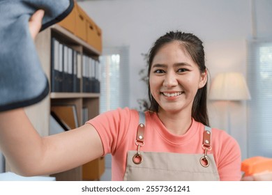 Happy cleaning lady wearing apron holding spray bottle and microfiber cloth, wiping dust from office shelf - Powered by Shutterstock