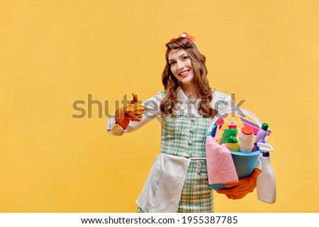 Happy cleaning woman with cleaning tools in the house shows a super gesture, thumbs up. A bottle of household chemicals and cleaning products. Pin-up style. Yellow background.