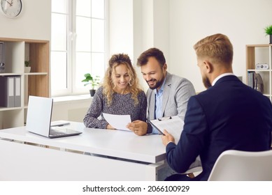 Happy clients sitting at desk in real estate agent's office and reading papers that he gave them. Young married couple who are planning to buy new house reading contract terms and conditions together