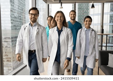 Happy clinic diverse team in medical professional uniforms walking in clinic office hall, looking at camera, smiling, laughing. Confident young ambitious doctors posing for front portrait - Powered by Shutterstock