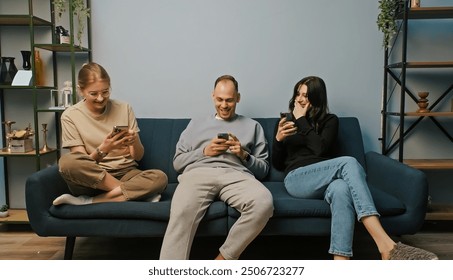 Happy close friends enjoying time together playing with their phones in cozy setting. Deeply immersed in digital world. Excited expression sitting on sofa. Modern social interactions concept - Powered by Shutterstock