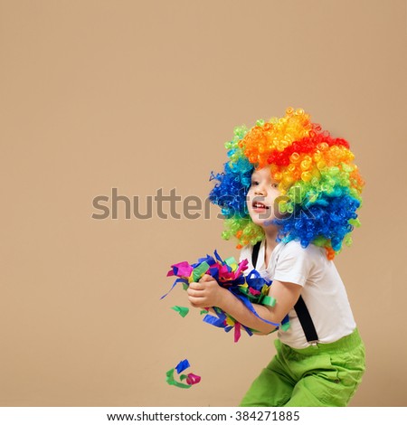 Happy clown boy with large colorful wig. Little boy in clown wig jumping and having fun. Portrait of a child throws up a multi-colored tinsel and confetti. Brazilian Carnival. Venice Carnival.