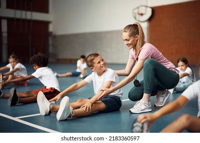 Happy coach assisting her student with stretching exercise during physical education class at school gym - Powered by Shutterstock