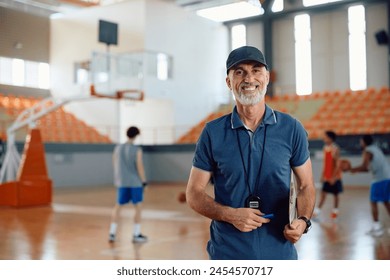 Happy coach with basketball players in the background looking at camera. Copy space. - Powered by Shutterstock