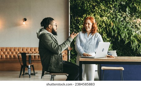 Happy colleagues collaborating in a vibrant cafe, discussing and using a laptop for a project. Professionals in the tech industry exemplify successful teamwork and remote work in a coworking space. - Powered by Shutterstock