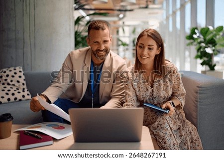 Happy colleagues cooperating while analyzing business reports and using laptop in the office. 