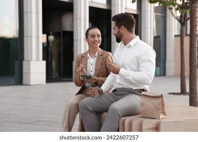 Happy colleagues having business lunch together on bench outdoors - Powered by Shutterstock