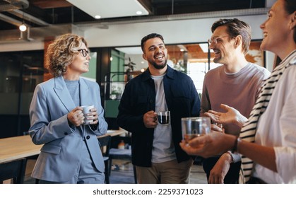 Happy colleagues having a coffee break in an office. Group of business people having a conversation in a workplace. Business professionals working in a startup. - Shutterstock ID 2259371023
