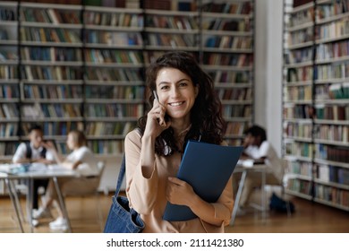 Happy college Latin student talking on mobile phone in university library, looking at camera with toothy smile, making telephone call from campus, discussing study research project. Head shot portrait - Shutterstock ID 2111421380