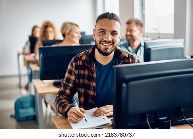 Happy college student attending computer class and taking notes while looking at camera.