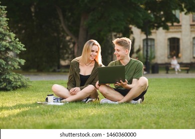 Happy college students communicating, talking, using laptop on campus lawn. Young cheerful caucasian couple of students watching videos on computer, looking at the screen in the university park.