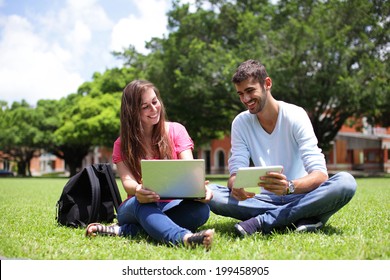 Happy College students using laptop and tablet pc on campus lawn, caucasian