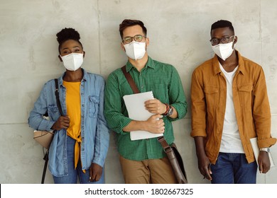 Happy College Students Wearing Protective Face Masks Ang Looking At Camera While Standing Against The Wall. 