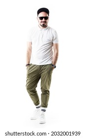 Happy Comfortable Stylish Young Man Wearing Chino Pants Cap And Sunglasses Smiling. Full Length Portrait Isolated On White Background