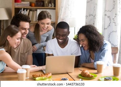 Happy company of diverse male and female young friends sitting at table in cafe with computer, laughing at funny videos or comedy movie using wifi, watching party photos, enjoying free time together. - Shutterstock ID 1443736133