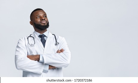 Happy confident african american medical doctor in white uniform looking at copy space, white studio background, panorama