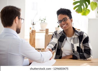 Happy confident applicant of African descent shaking the hand of an HR manager offering a new job. A black candidate getting hired at job interview/handshaking with client at meeting/making a good first impression. Employment concept