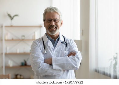 Happy confident bearded old professional doctor standing arms crossed looking at camera. Smiling senior adult physician, reliable successful therapist wearing white lab coat and stethoscope, portrait.