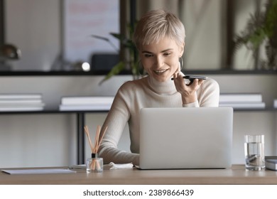 Happy confident business woman recording audio message on smartphone, making phone call on speaker at workplace in office, giving audio command to virtual assistant, using voice recognition app - Powered by Shutterstock