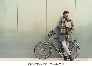 Happy confident businessman concentrating on his online work on the fintech device while standing in the city next to his bike. Photo with copy space of cheerful businessman with digital tablet. - Powered by Shutterstock