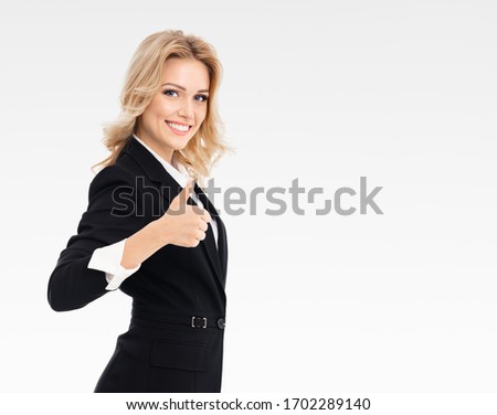 Happy confident businesswoman showing thumbs up gesture, on grey background, with blank copyspace area for slogan or text message. Caucasian model in business presentation concept. 