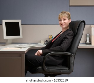 Happy, Confident Businesswoman Sitting At Desk In Cubicle