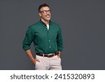 Happy confident cool middle aged business man, smiling mature professional businessman wearing green shirt and stylish eyeglasses looking aside standing isolated on gray background.