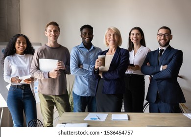 Happy confident diverse old and young business people stand together in office, smiling multiethnic professional colleagues staff group look at camera, human resource concept, team corporate portrait