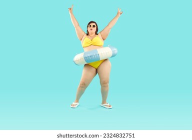 Happy confident fat woman having fun at beach party on summer vacation holiday. Plus size lady in yellow bikini, with inflatable rubber floater around waist dancing isolated on blue background - Powered by Shutterstock