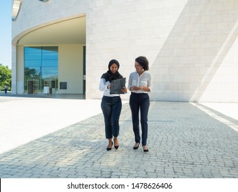 Happy Confident Female Business Partners Discussing Contract Outside. Multiethnic Women In Office Suits And Hijab Walking Outside And Carrying Folder With Documents. Partners Concept