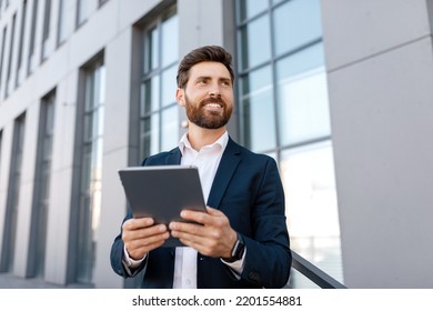 Happy Confident Handsome Young Caucasian Man With Beard In Suit Typing On Tablet, Look At Empty Space Near Office Building. Successful Business Outdoor, Businessman Uses App For Trade, Ad And Offer