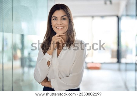 Happy confident Latin professional mid aged business woman in office, portrait. Smiling lady corporate leader, mature female executive, lady manager standing in looking at camera, portrait.