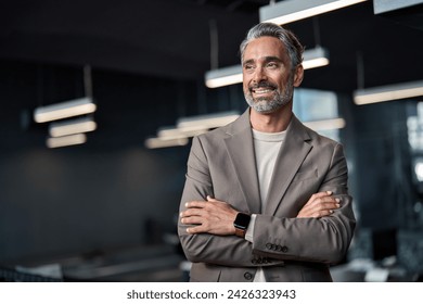 Happy confident mature 45 years old business man investor standing in office looking away. Middle aged rich business owner male ceo executive leader wearing suit at work thinking on future success.