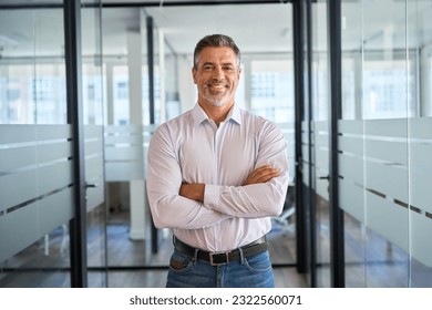 Happy confident mature latin business man standing in office hall, portrait. Smiling mid aged older corporate manager, successful professional executive investor looking at camera with arms crossed.
