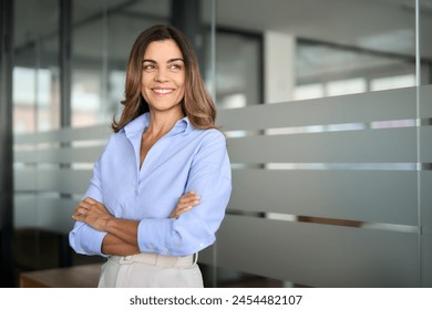 Happy confident mature professional business woman standing at work in office arms crossed looking away, proud hispanic middle aged businesswoman leader executive thinking of future success.