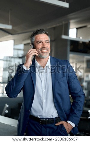 Happy confident middle aged business man talking on mobile phone in office. Successful professional businessman executive entrepreneur wearing suit holding telephone making corporate call on cell.